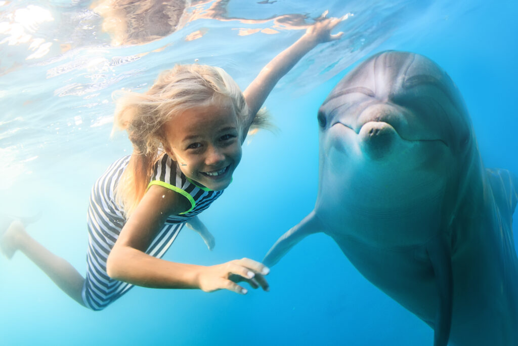 Blonde seven-year-old girl diving with dolphin.