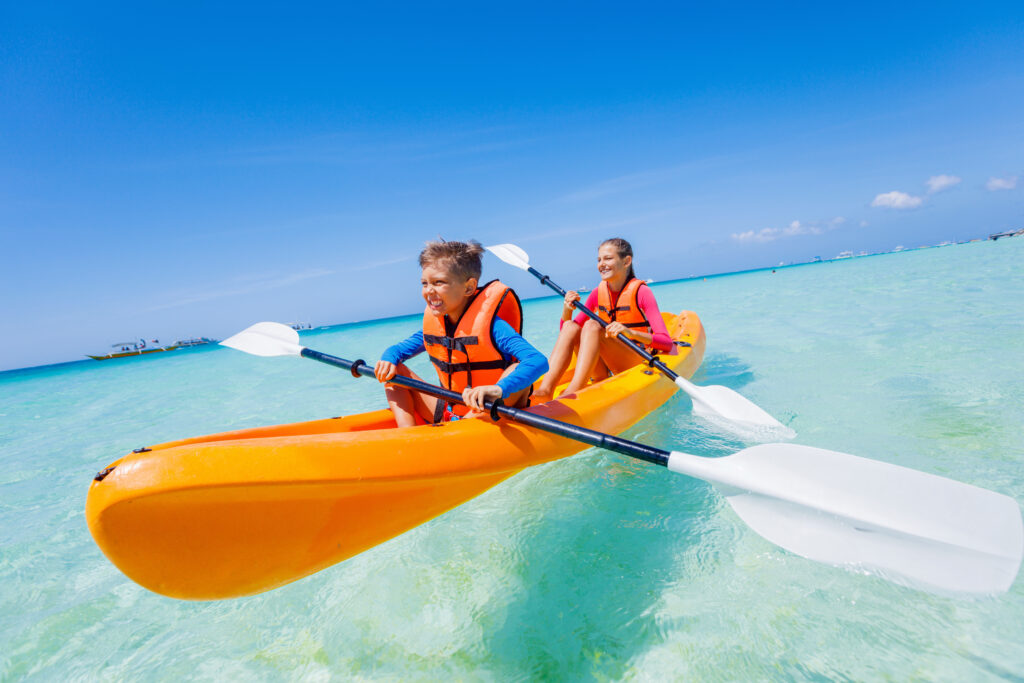 Boy and girl riding an orange kayak on the ocean